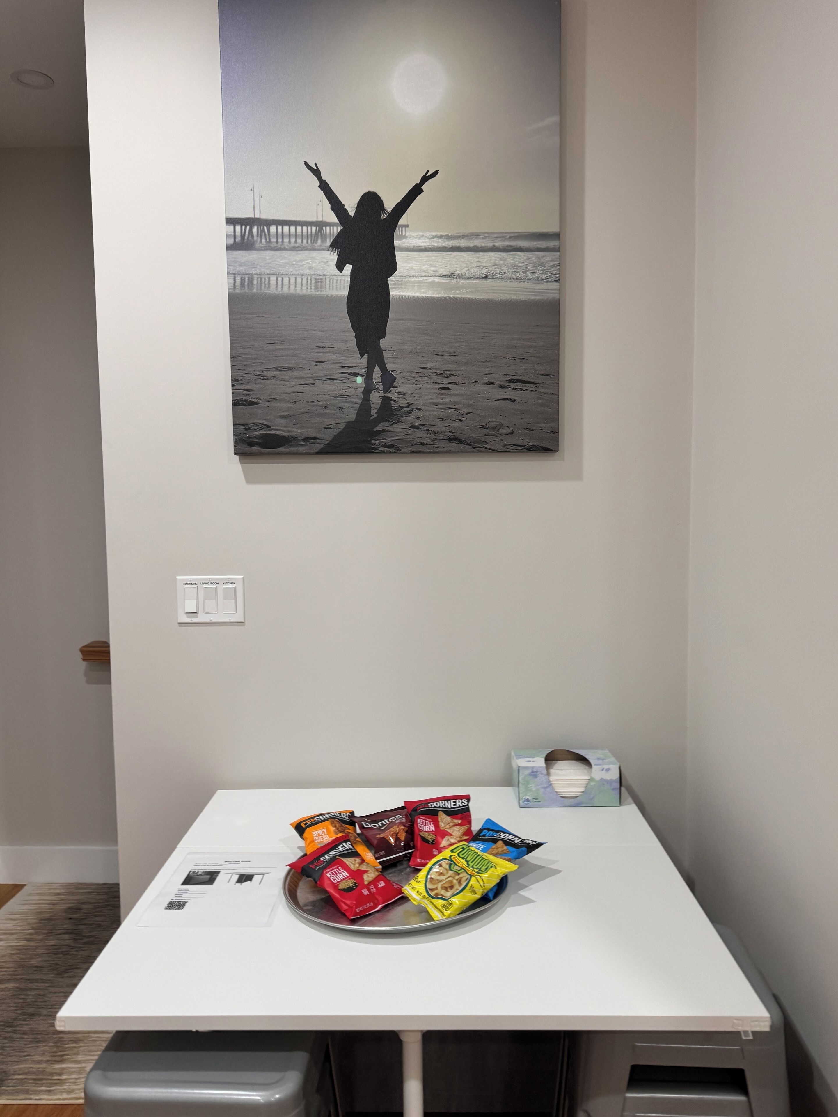 Een kamer met een witte tafel waarop snacks en een lijst met een foto van iemand op het strand staan.