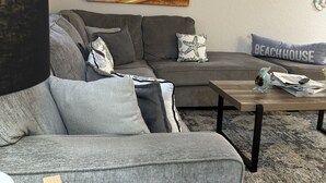 A modern living room with a grey sectional sofa, a wooden coffee table, and a painting of a sunset over the ocean.