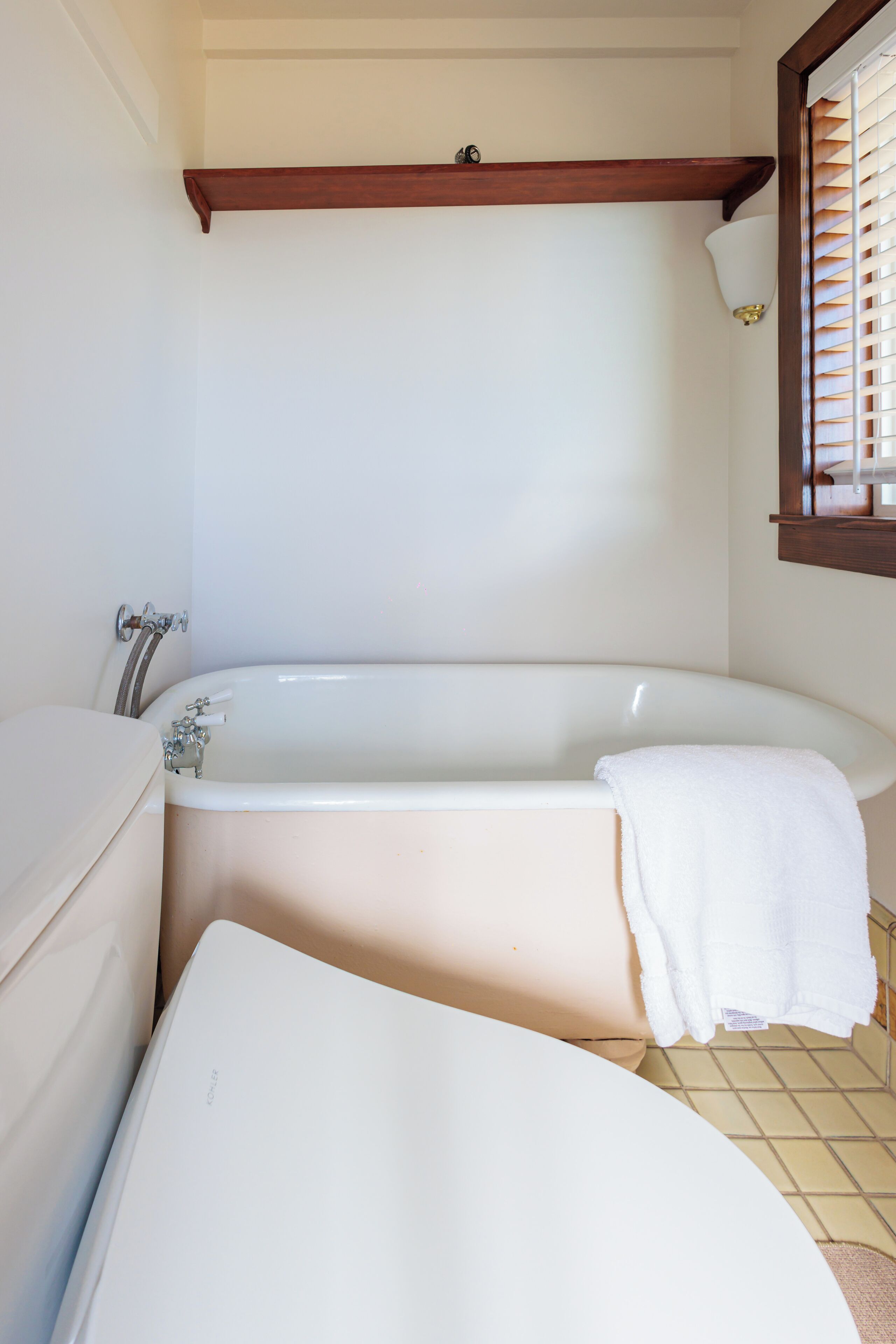 A bathroom with a bathtub, a toilet, and a window with blinds.