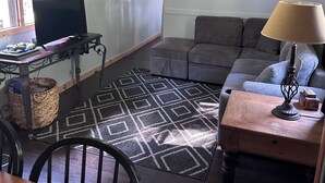 A living room with a sofa, a table with a lamp, a TV on a stand, a patterned rug, and a window with curtains. - Private & Cozy! Close to the Clarion River & State Parks!- Camp Harv est.1994 (Clarington)