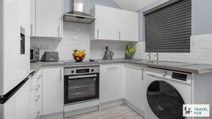 A modern kitchen with white cabinets, a built-in oven, a washing machine, and a window with blinds.