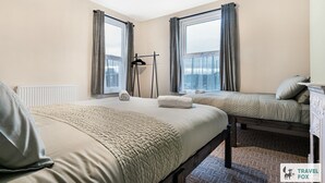 A hotel room with two beds, a radiator, a hanging light fixture, and a view of the city.