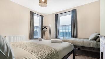 A hotel room with two beds, a radiator, a hanging light fixture, and a view of the city.