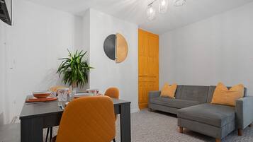 Una sala de estar moderna con un sofá gris, cojines naranjas y un comedor con una mesa dispuesta para dos.