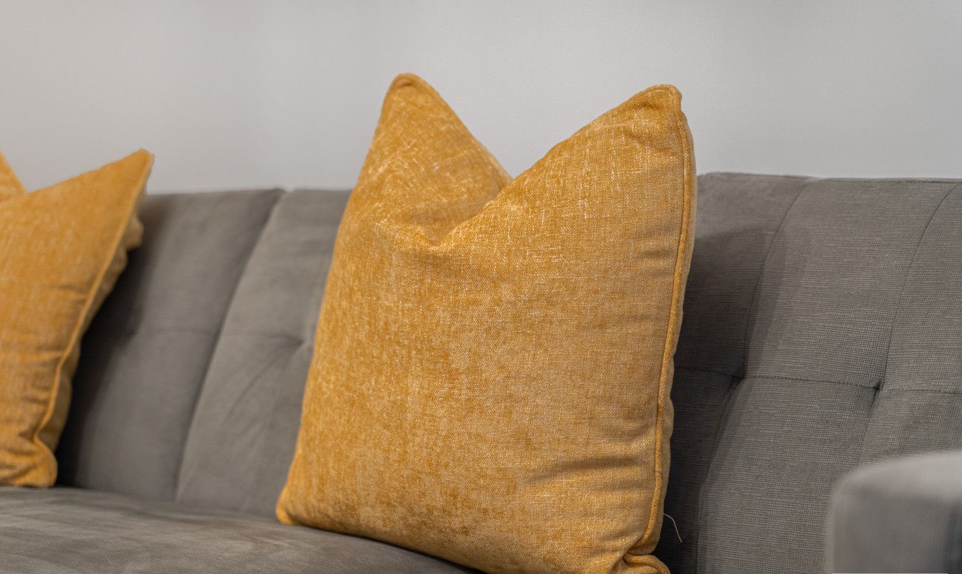 A grey sofa with two mustard-colored pillows.