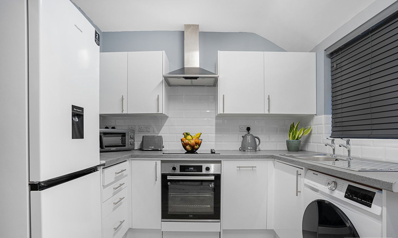 A modern kitchen with white cabinetry, a built-in oven, a microwave, and a coffee maker.