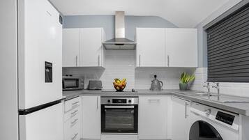 A modern kitchen with white cabinetry, a built-in oven, a microwave, and a coffee maker.