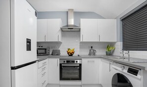 Eine moderne Küche mit weißen Schränken, einem Backofen, einer Mikrowelle und einer Kaffeemaschine.