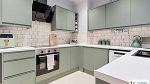 Una cucina moderna con mobili verde chiaro, un piano di lavoro bianco, un forno integrato e un bollitore.
