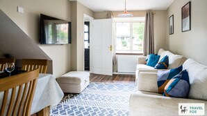 A cozy living room with a sofa, a TV mounted on the wall, a dining table with chairs, and a patterned rug. - Lily's Stay Central  Parking (Nottingham)