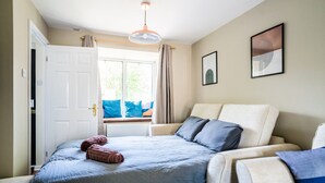 A bedroom with a bed, a chair, a window with curtains, and a ceiling light. - Lily's Stay Central  Parking (Nottingham)