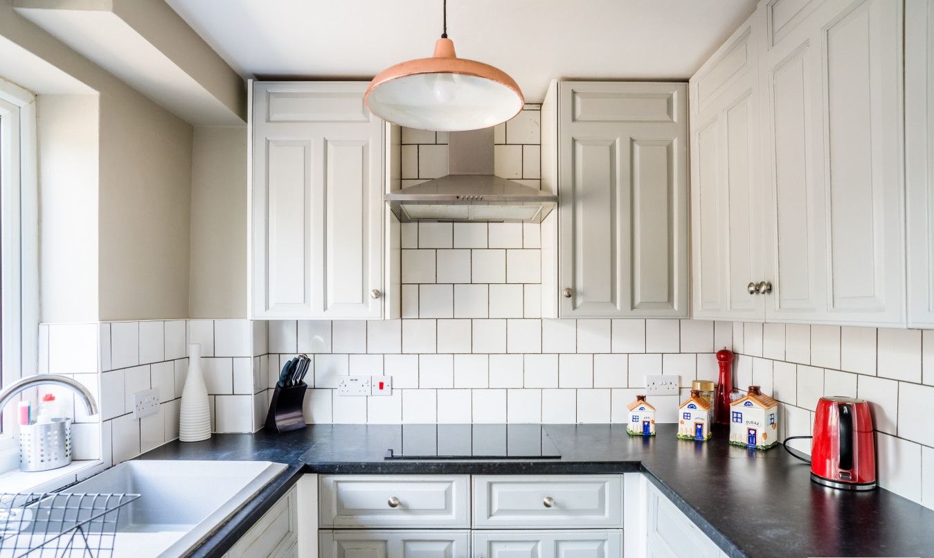 A kitchen with white cabinets, a black countertop, a hanging light, and a coffee maker.