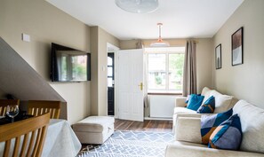 Een gezellige woonkamer met een bank, een aan de muur bevestigde televisie, een eettafel met stoelen en een kamerkleed met dessin.