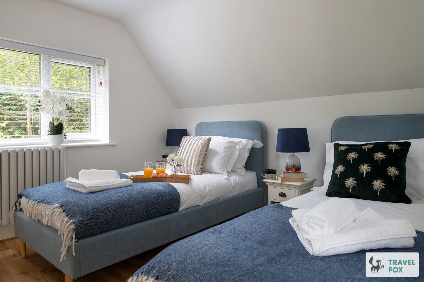 Ein Schlafzimmer mit zwei Betten, einem Fenster mit Blick auf Grünflächen, einem Heizkörper und einem Tablett mit Frühstücksangeboten.