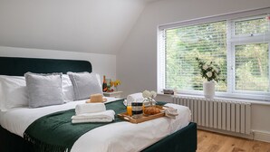A neatly made bed with a green bedspread, white linens, and a tray with breakfast items. A window with blinds and a view of greenery is visible. - Orchard Cottage and Hot Tubs (Snowdonia & North Wales)