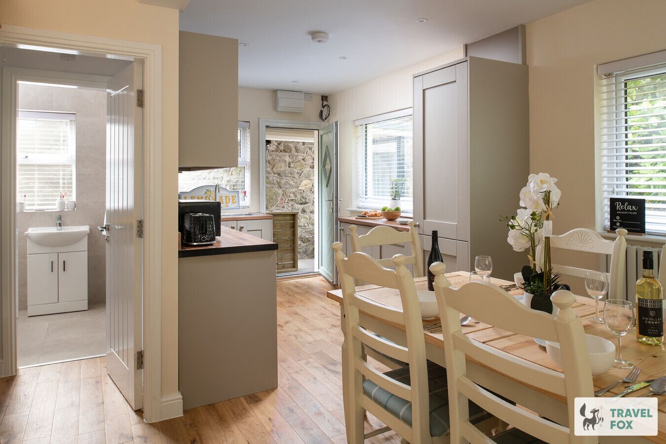 A modern kitchen with a dining area, featuring a stone backsplash, wooden cabinets, and a dining table set for two.