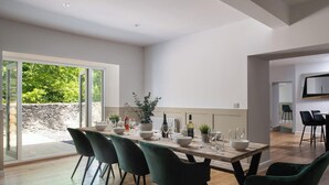 A modern dining area with a wooden table, green chairs, and a view of greenery outside. - Orchard Cottage and Hot Tubs (Snowdonia & North Wales)