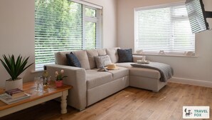 A cozy living room with a beige sectional sofa, a wooden coffee table with books and glasses, and a potted plant. - Orchard Cottage and Hot Tubs (Snowdonia & North Wales)