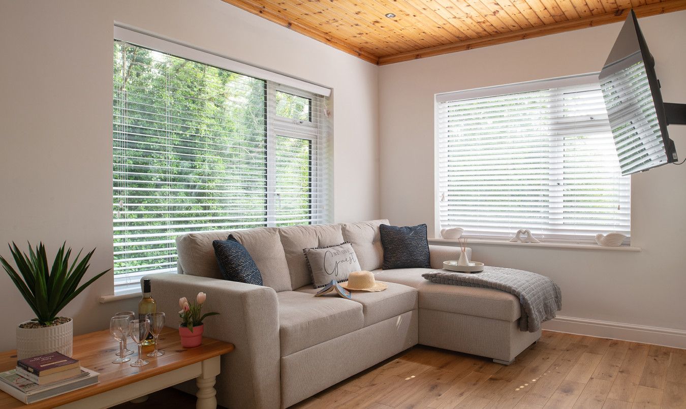 A cozy living room with a beige sectional sofa, a wooden coffee table with books and glasses, and a potted plant.