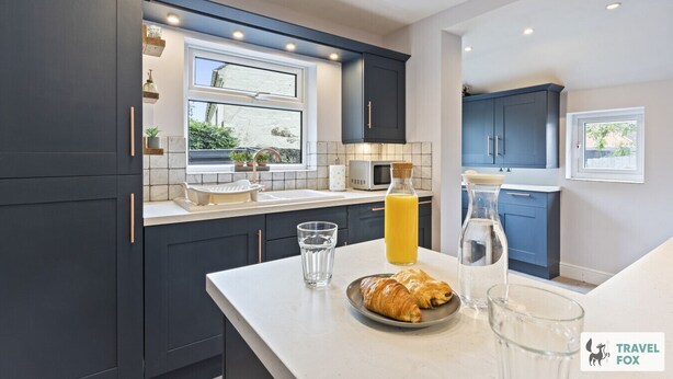 A modern kitchen with dark cabinets, a white countertop, a window, and a breakfast setup including croissants and juice.