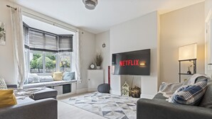 A modern living room with a large flat-screen TV mounted on the wall, a comfortable sofa, a bench with cushions, and a patterned rug.