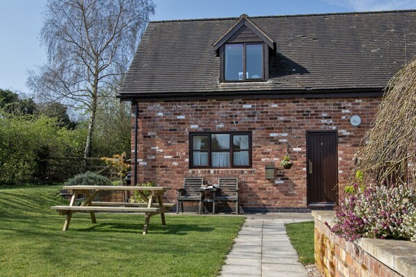 A brick house with a sloped roof, a small porch, and a wooden bench in the yard.