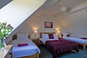A room with two beds, a wooden headboard, bedside tables, a vase with flowers, and a painting on the wall.
