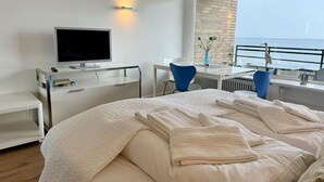 Een moderne hotelkamer met een groot bed, een bureau met een computer, een televisie en uitzicht op zee.
