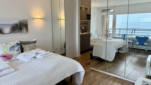 Een moderne hotelkamer met twee bedden, een grote spiegel, een kitchenette en een balkon met uitzicht.