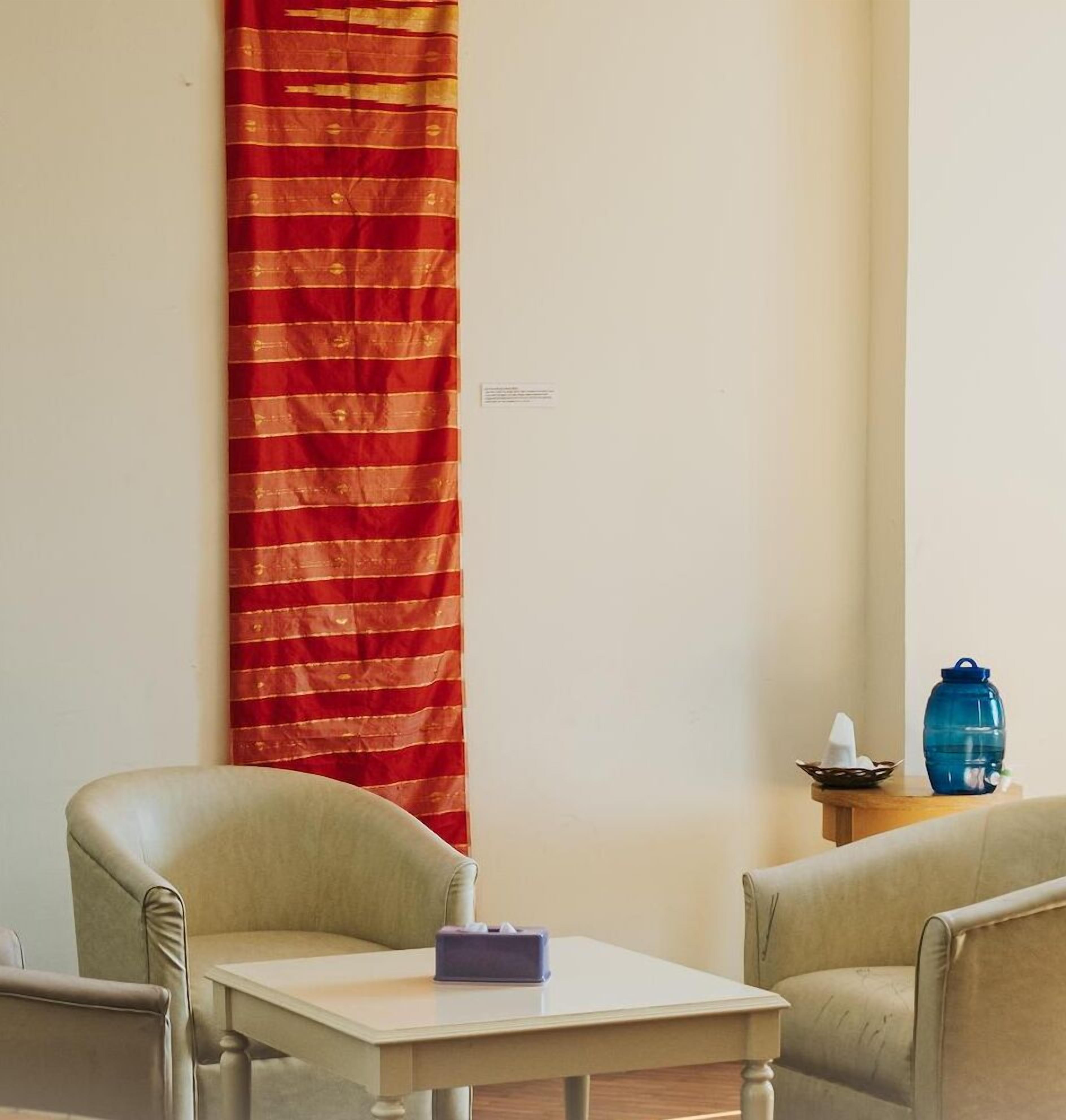 A room with two armchairs, a small table, a blue water container, and a red curtain.