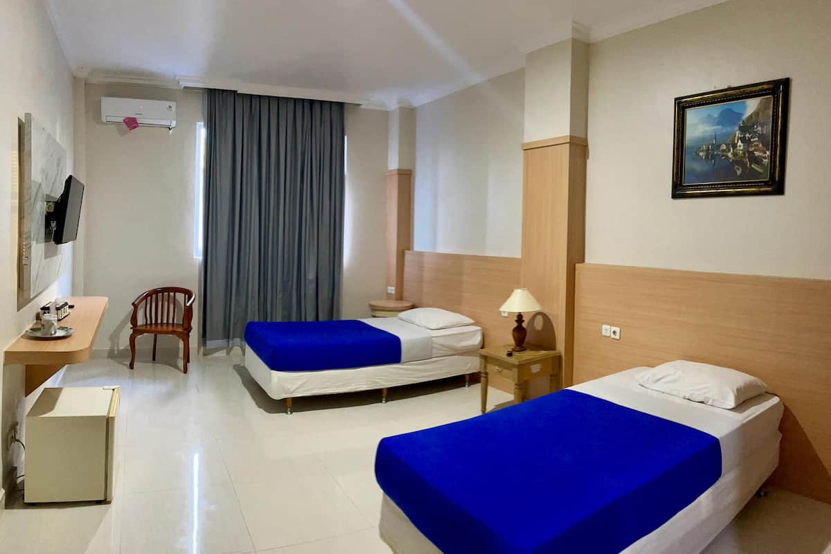 A hotel room with two beds, a desk, a chair, a lamp, and a painting on the wall.