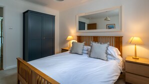 A bedroom with a bed, two bedside tables, a nightstand, a wardrobe, a mirror, and a hanging light fixture.