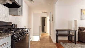 Uma cozinha moderna com fogão a gás, soalho de madeira e um corredor que leva a uma sala de estar com um sofá.