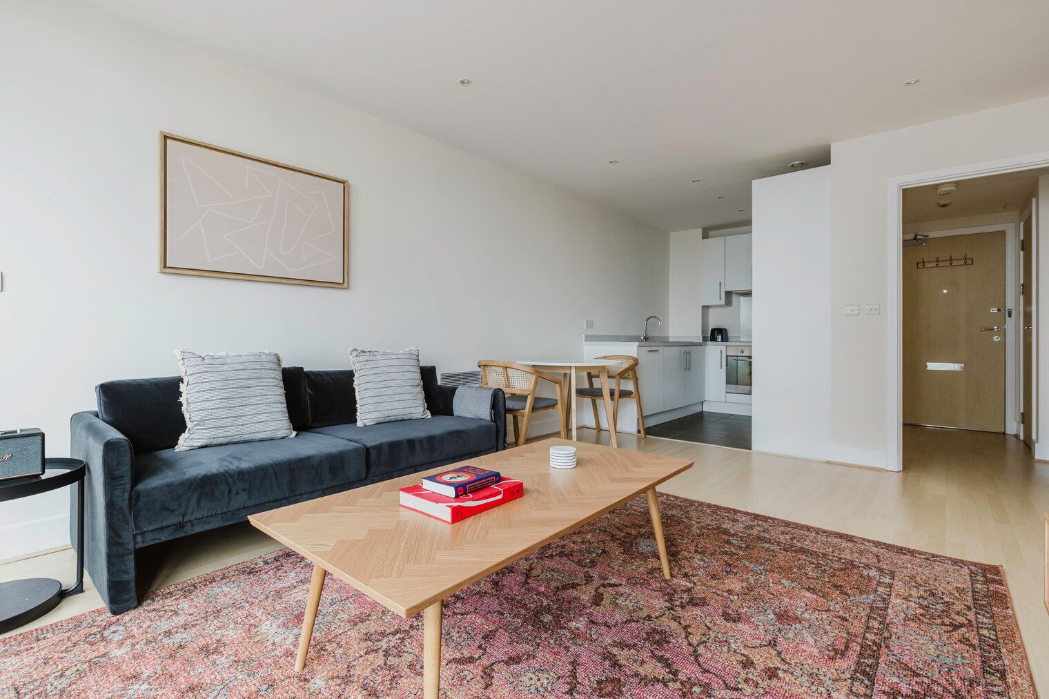 A modern living room with a dark blue sofa, a wooden coffee table with books, and a patterned rug.