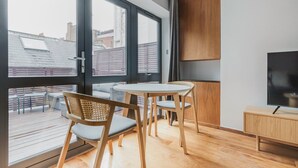 Un salon moderne avec une grande fenêtre, une table ronde, deux chaises, un téléviseur et un meuble en bois.