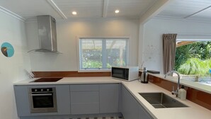Eine kompakte Küche mit Mikrowelle, Backofen und Spüle. Ein Fenster mit Jalousien, ein dekoratives Wandbild und ein fußbodenbelag mit Muster sind vorhanden.