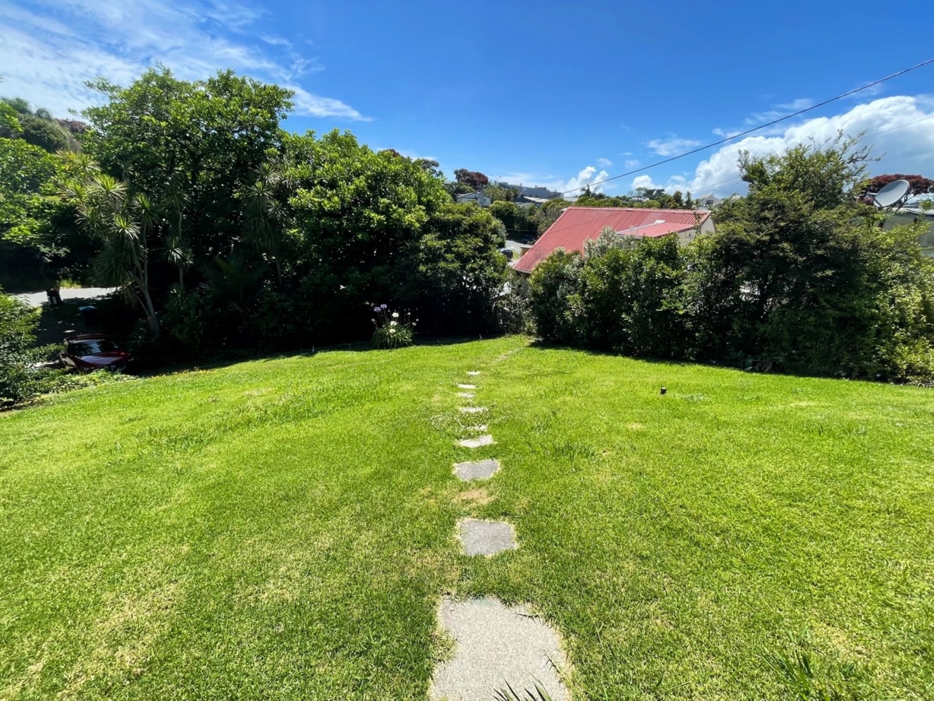 A grassy yard with a stone pathway leading to a building with a red roof.