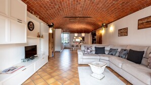 Un espacio habitable amplio con techo de ladrillo, muebles blancos y una zona de comedor al fondo.