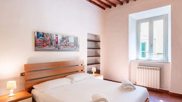 Ein Schlafzimmer mit einem Bett, einem Nachttisch, einem Fenster, einer Heizung und einem Bild an der Wand.