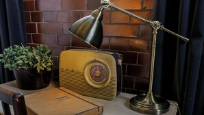 A vintage radio, a lamp, and a potted plant on a table against a brick wall. - Betts Private room at Bicester Heritage (Bicester)