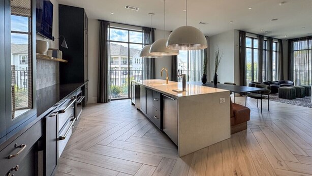 A modern kitchen with a central island, pendant lights, and large windows offering views of the outdoors.