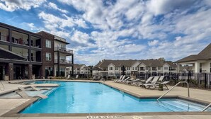 A swimming pool with lounge chairs and a multi-story building in the background.