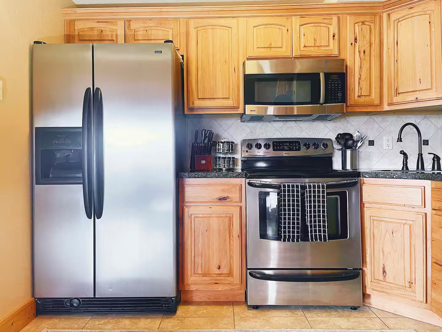 Une cuisine équipée d’un réfrigérateur en acier inoxydable, d’un four à micro-ondes, d’une cuisinière et de meubles de rangement en bois.