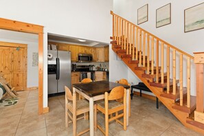 Una cocina con gabinetes de madera, un refrigerador de acero inoxidable, un microondas y un comedor con una mesa y sillas de madera.