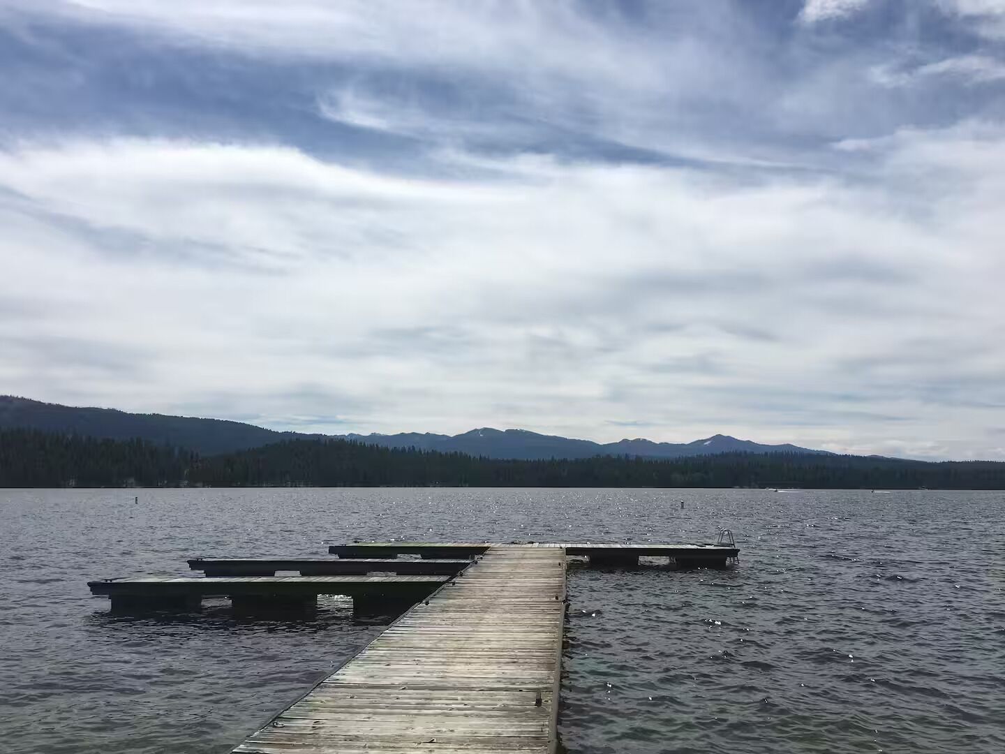 Een houten steiger die uitsteekt in een kalm meer, met bergen op de achtergrond.