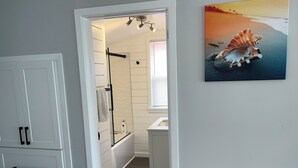 Une salle de bain avec une douche, un lavabo et des toilettes. On y trouve un porte-serviettes et un tableau représentant un coquillage accroché au mur.