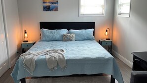 Une chambre à coucher comprenant un lit, deux tables de chevet, une commode, une fenêtre et un tableau accroché au mur.