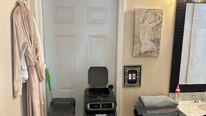 A compact bathroom with a shower, a towel rack, a drying rack, a sink, and a mirror.