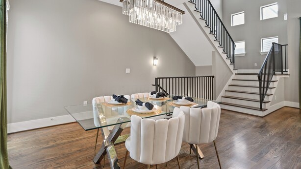 A dining area with a glass table, white chairs, a chandelier, and a staircase.