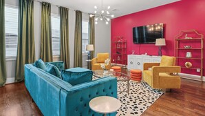 A living room with a blue sofa, yellow armchairs, a coffee table, and a TV on the wall.